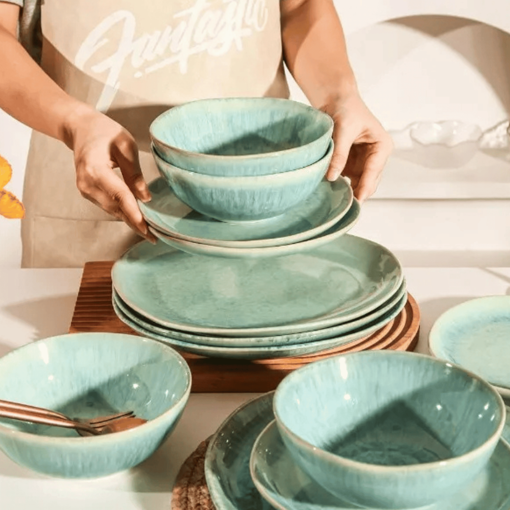 Person holding a stack of teal ceramic dishes on a table.