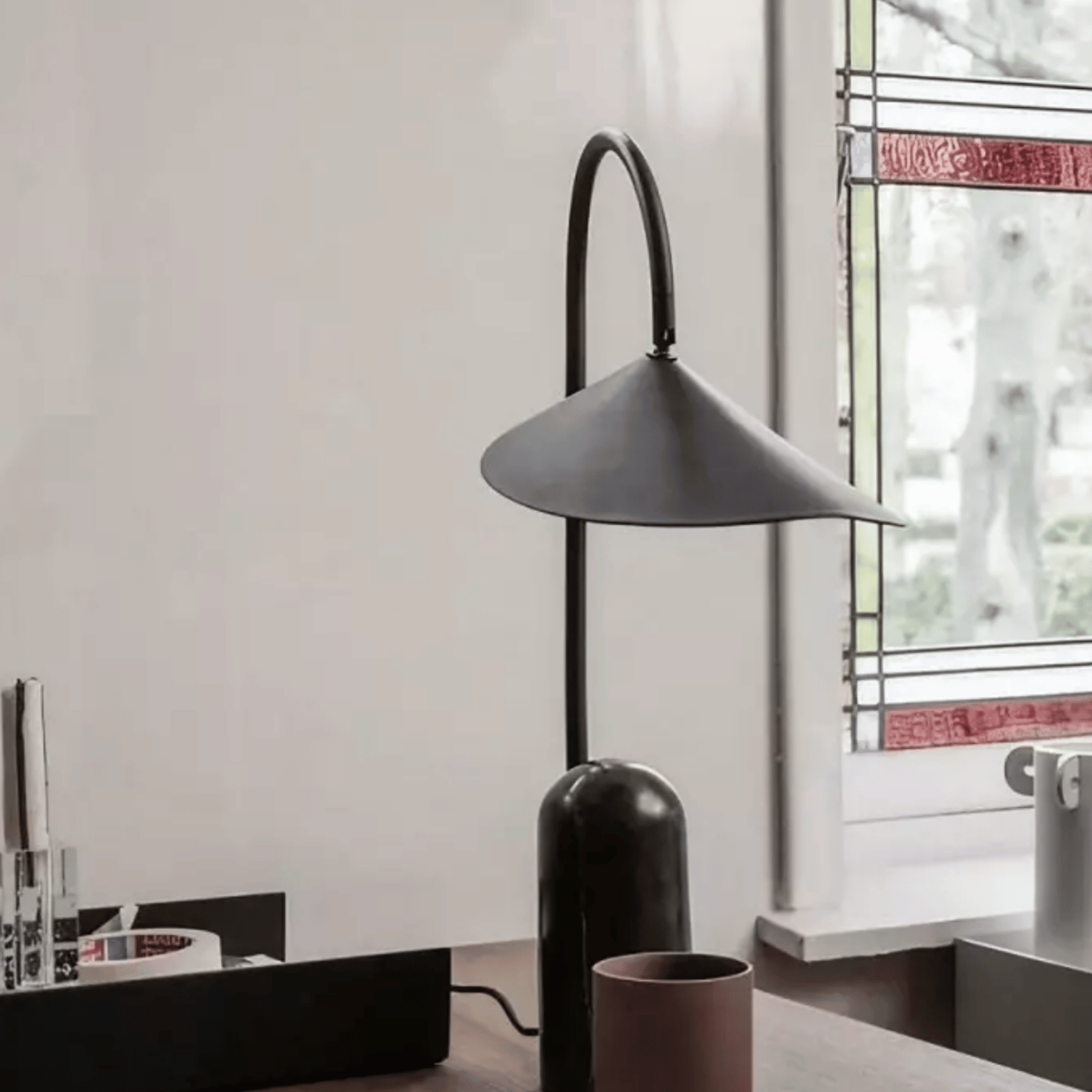 Modern black table lamp on a desk with a window in the background