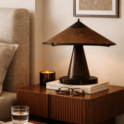 Decorative table lamp on a wooden side table with books and glasses in a cozy living room setting.