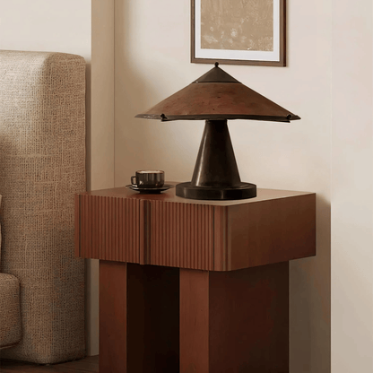 Decorative lamp on a wooden side table with a cup next to it, against a neutral wall.
