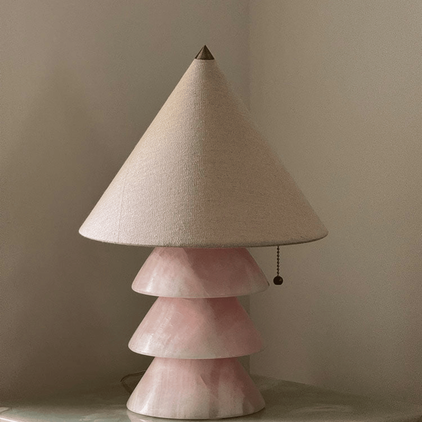 Table lamp with a cone-shaped beige lampshade and a pink ceramic base on a neutral background