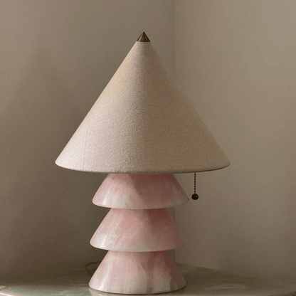 Table lamp with a cone-shaped beige lampshade and a pink ceramic base on a neutral background