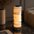 Decorative lamp with stacked circular design on a dark surface, next to a vase and a book.