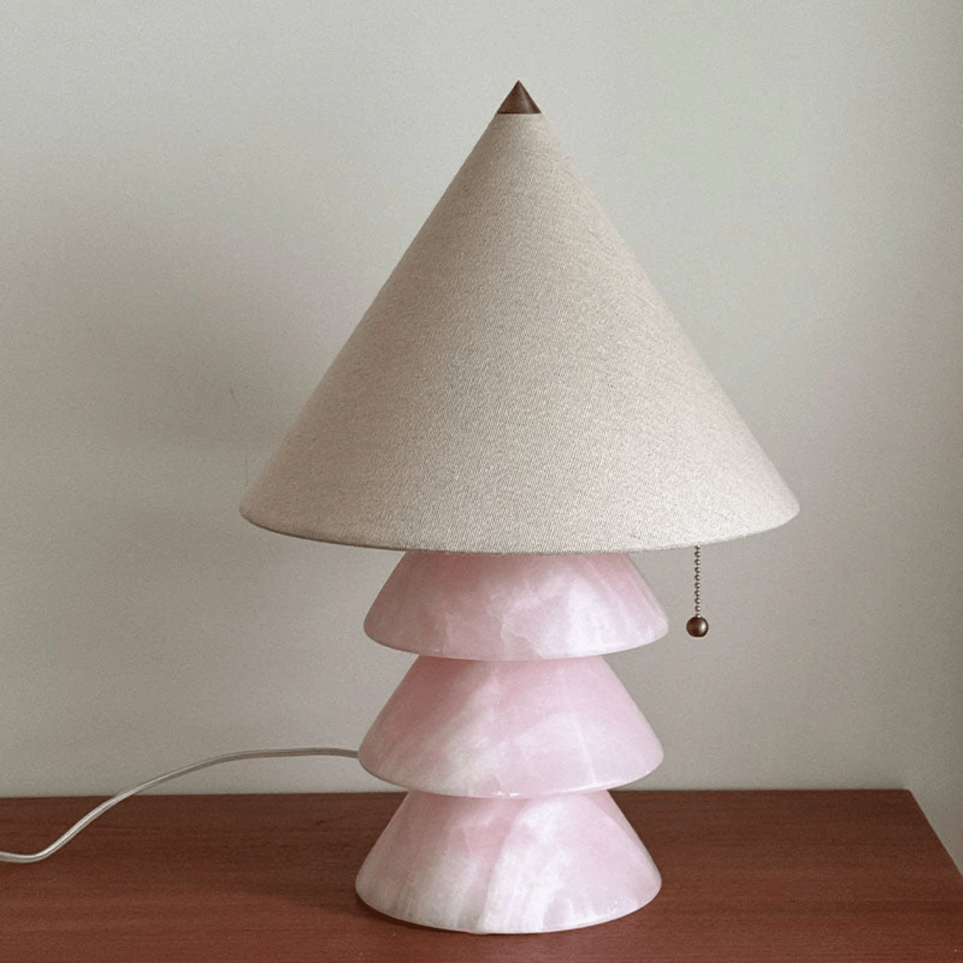 Table lamp with a pink base and beige cone-shaped shade on a wooden surface.