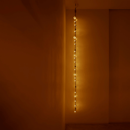 String of lights hanging vertically against a plain wall with warm lighting.