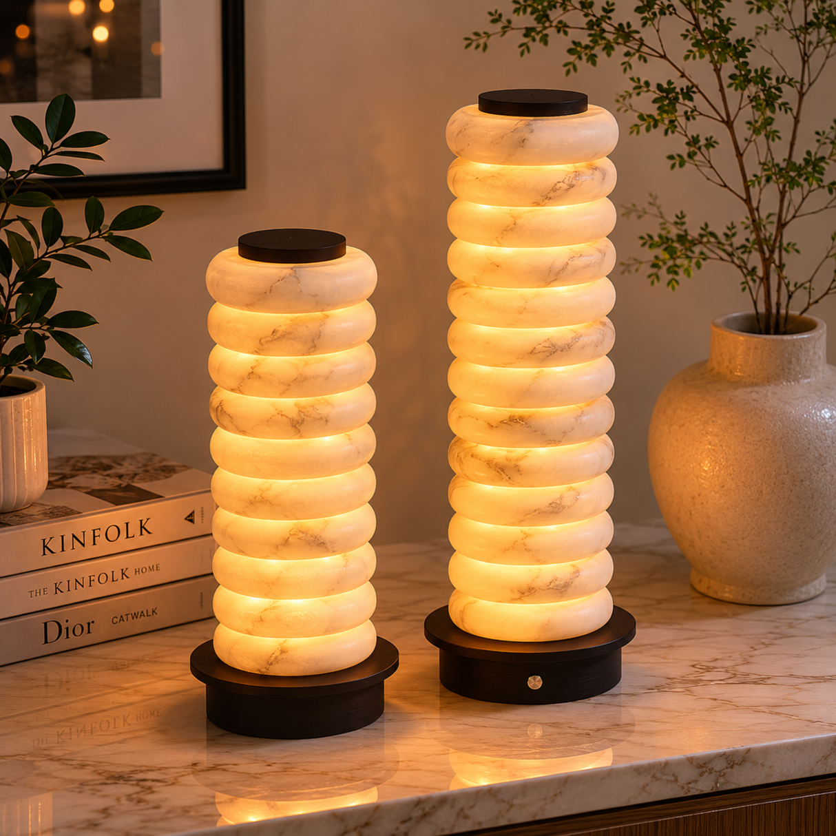 Two cylindrical lamps with a ribbed design on a marble surface, surrounded by books and decor items.
