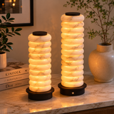 Two cylindrical lamps with a ribbed design on a marble surface, surrounded by books and decor items.
