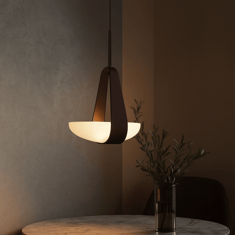 Modern pendant light hanging above a table with a vase of plants against a dark wall.