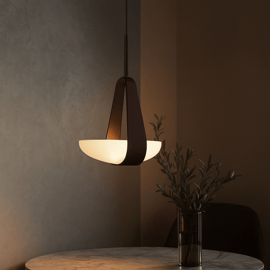 Modern pendant light hanging above a table with a vase of plants against a dark wall.