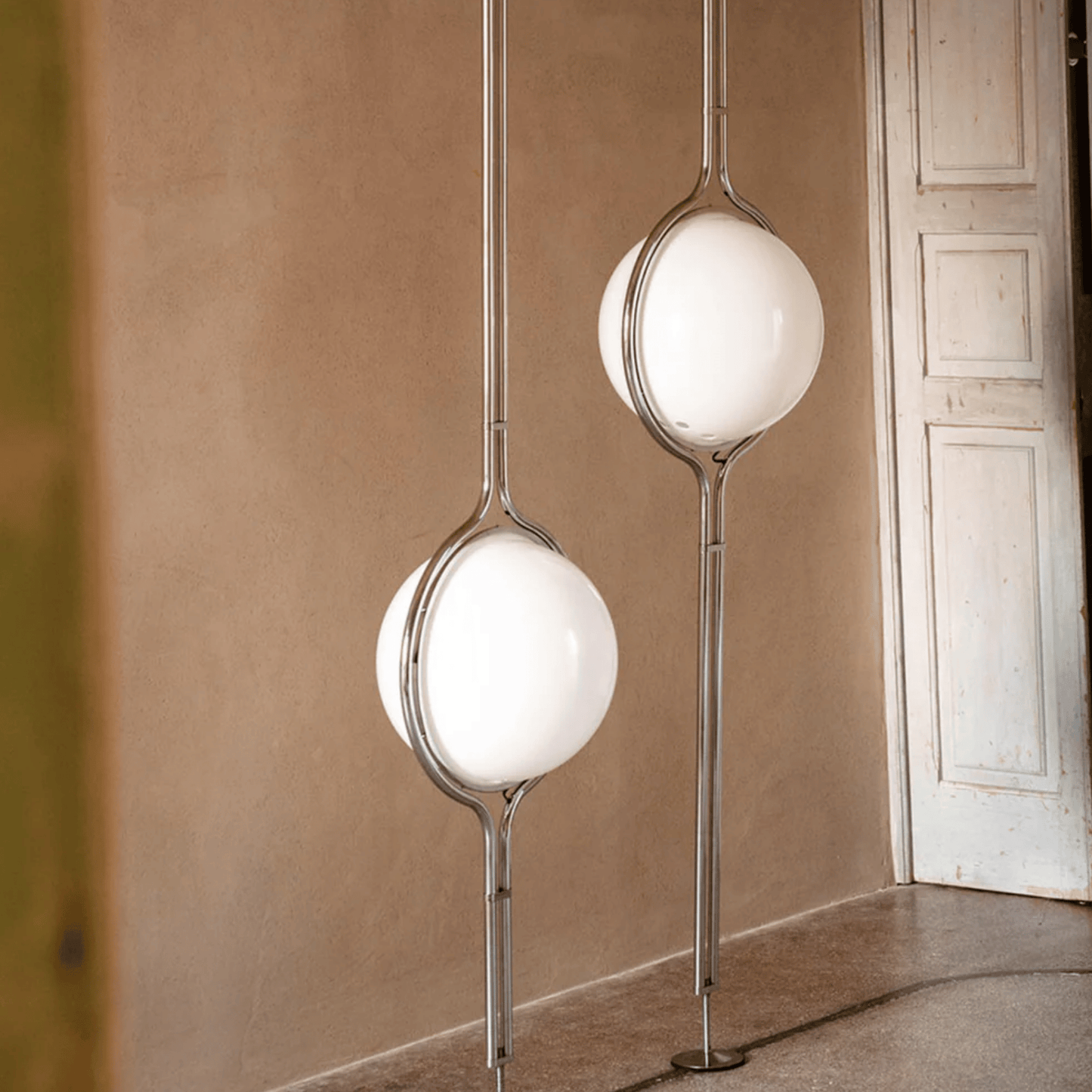 Modern floor lamps with spherical glass shades in a room with beige walls and a white door.