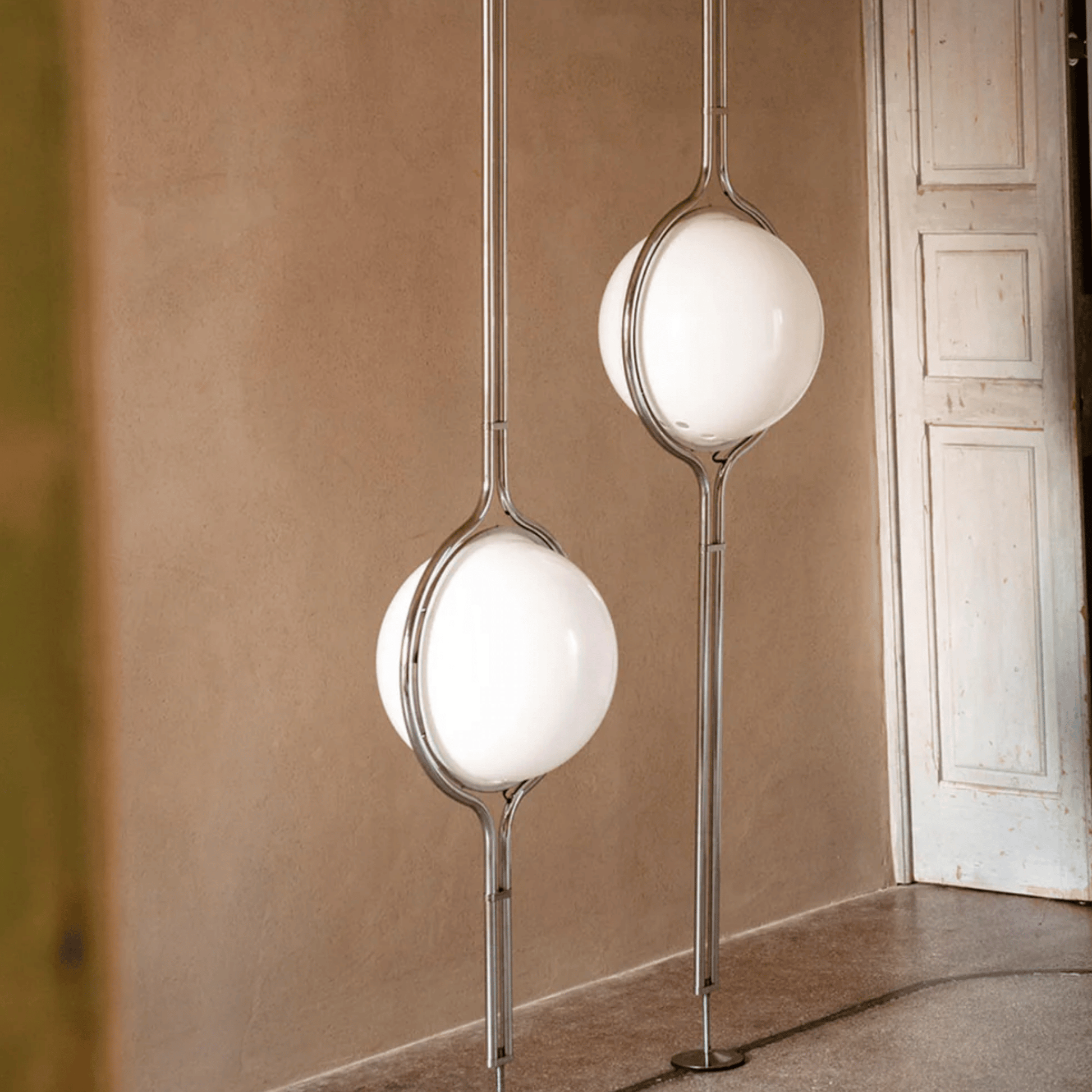 Modern floor lamps with spherical glass shades in a room with beige walls and a white door.