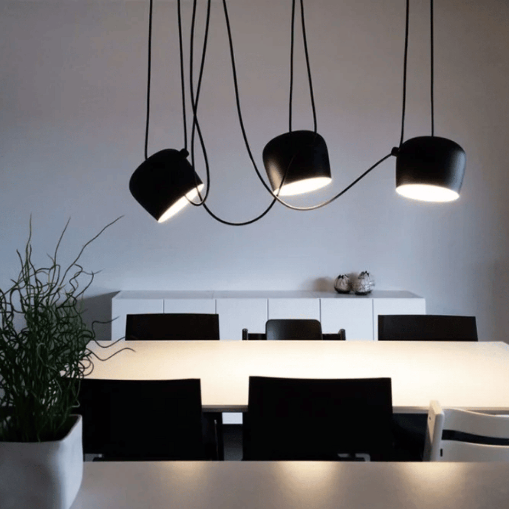 Modern black pendant lights hanging above a dining area with white walls and furniture.