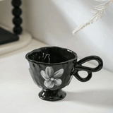 Black ceramic cup with floral design on a white surface
