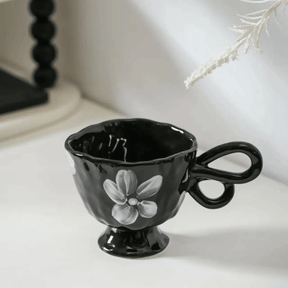 Black ceramic cup with floral design on a white surface