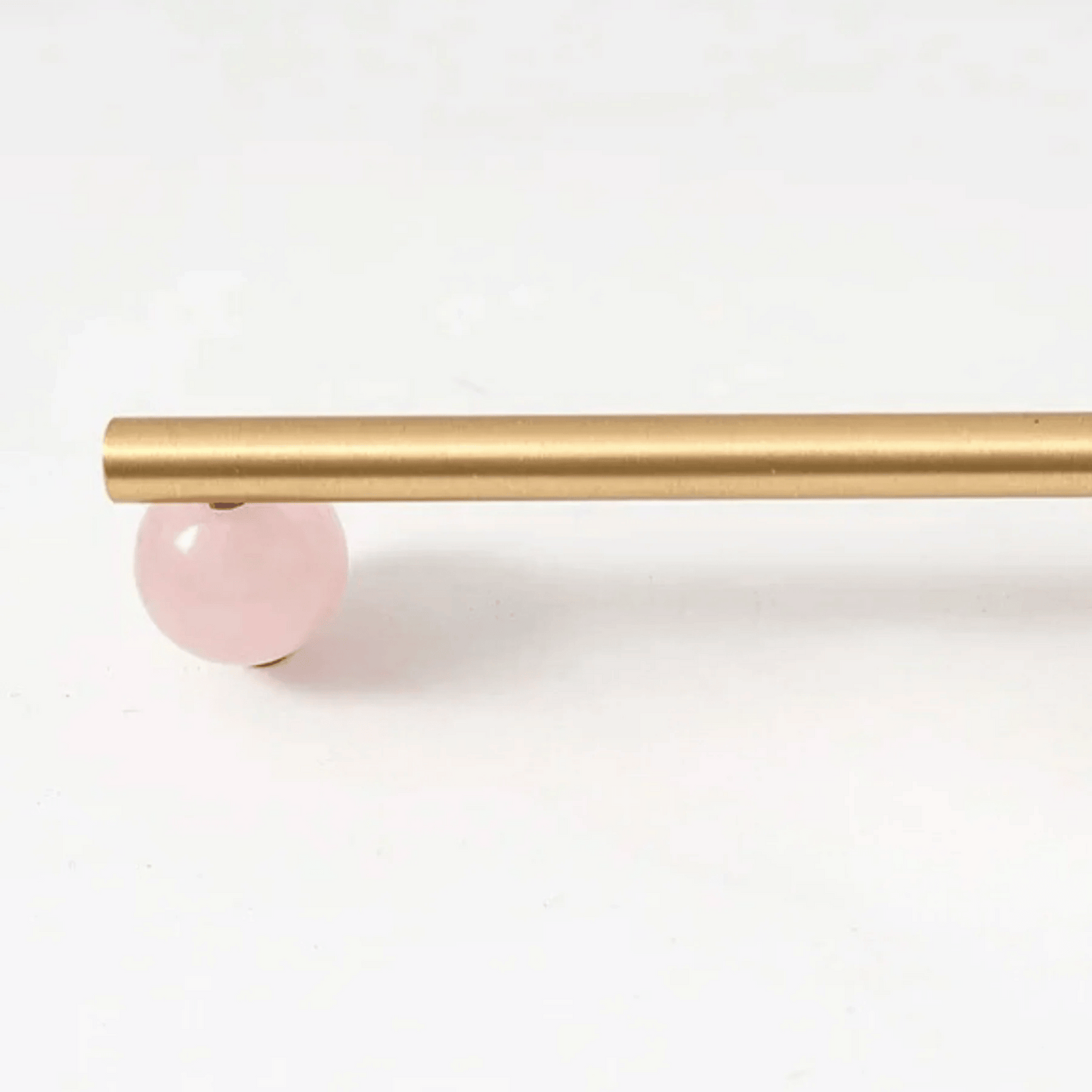 Gold curtain rod with a pink ball finial on a white background