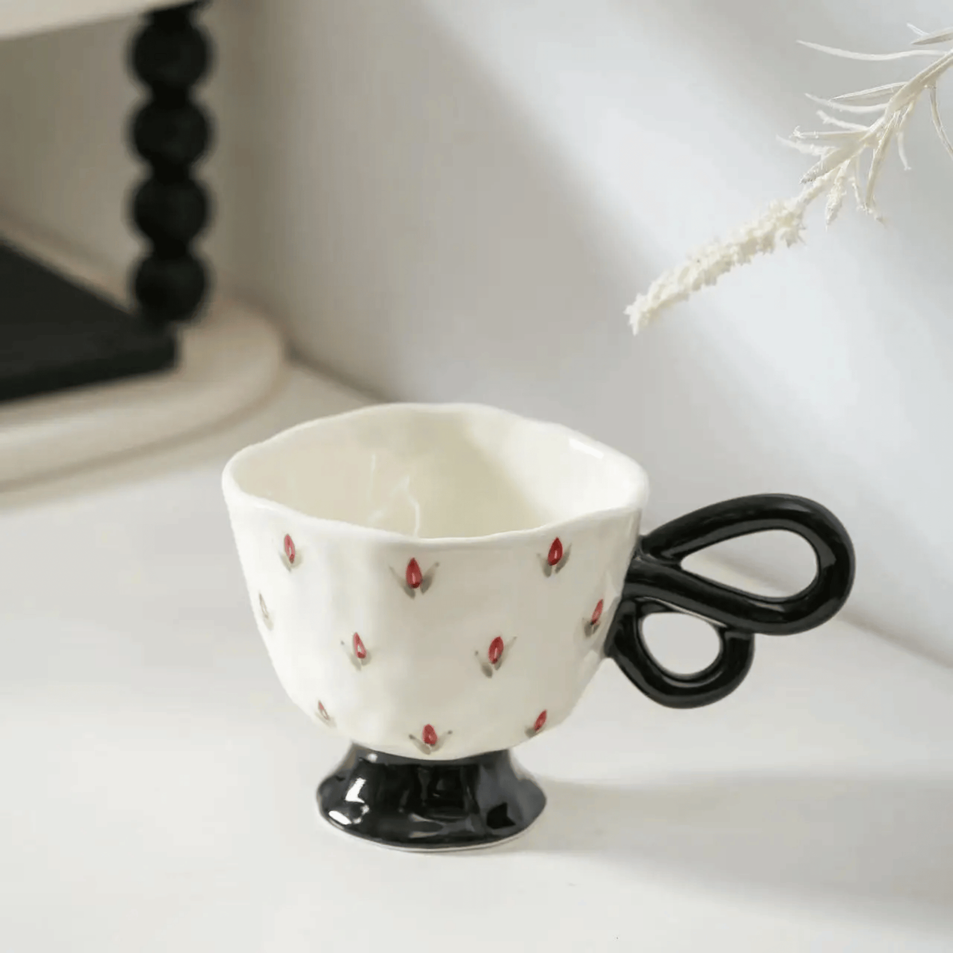 Ceramic cup with black handle resembling scissors on a white surface