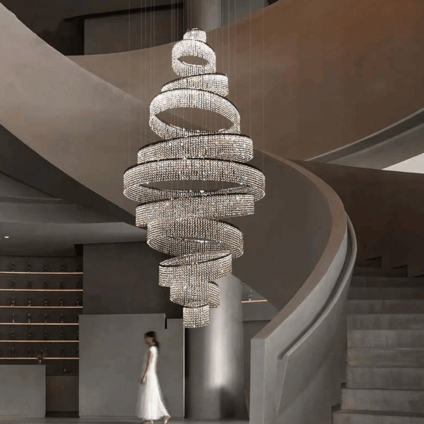 Large spiral chandelier hanging in a modern staircase setting with a woman in a white dress.