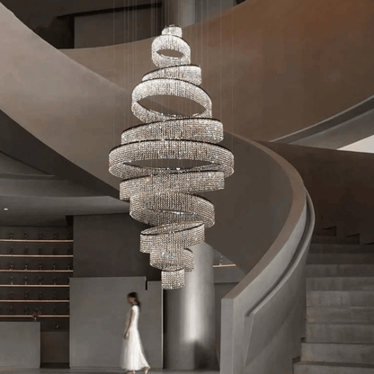 Large spiral chandelier hanging in a modern staircase setting with a woman in a white dress.
