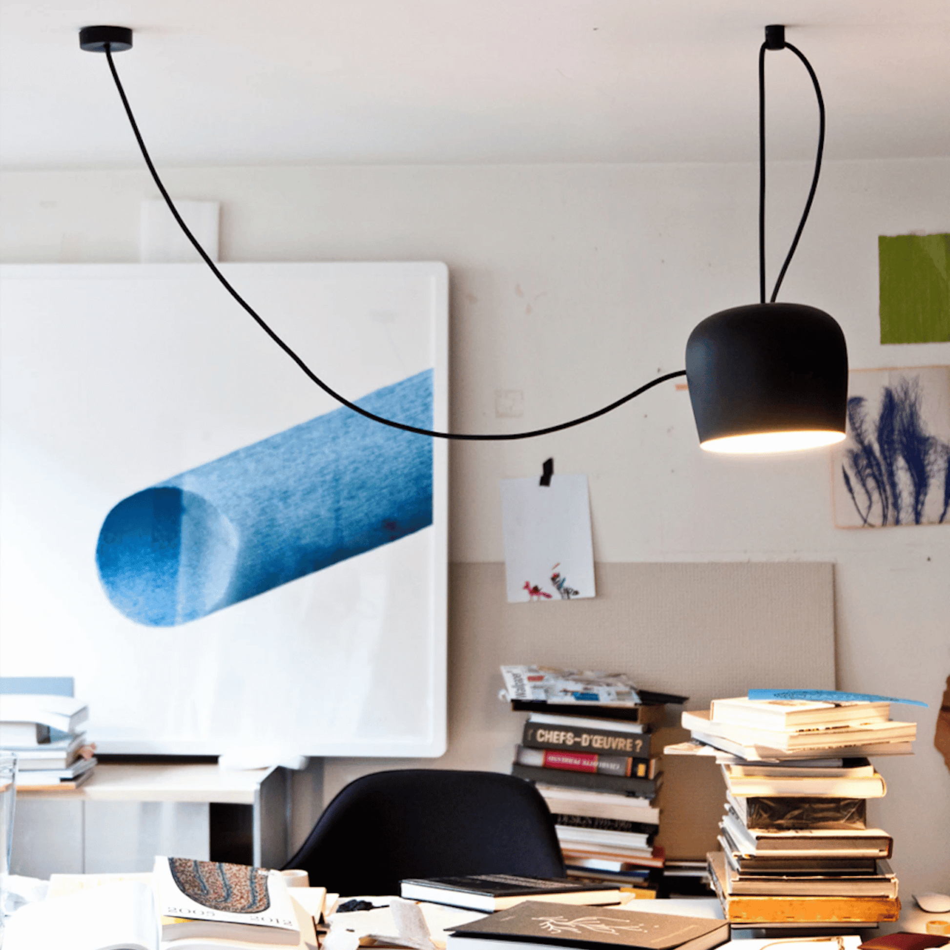 Modern office space with black pendant light, books, and artwork on a white wall.