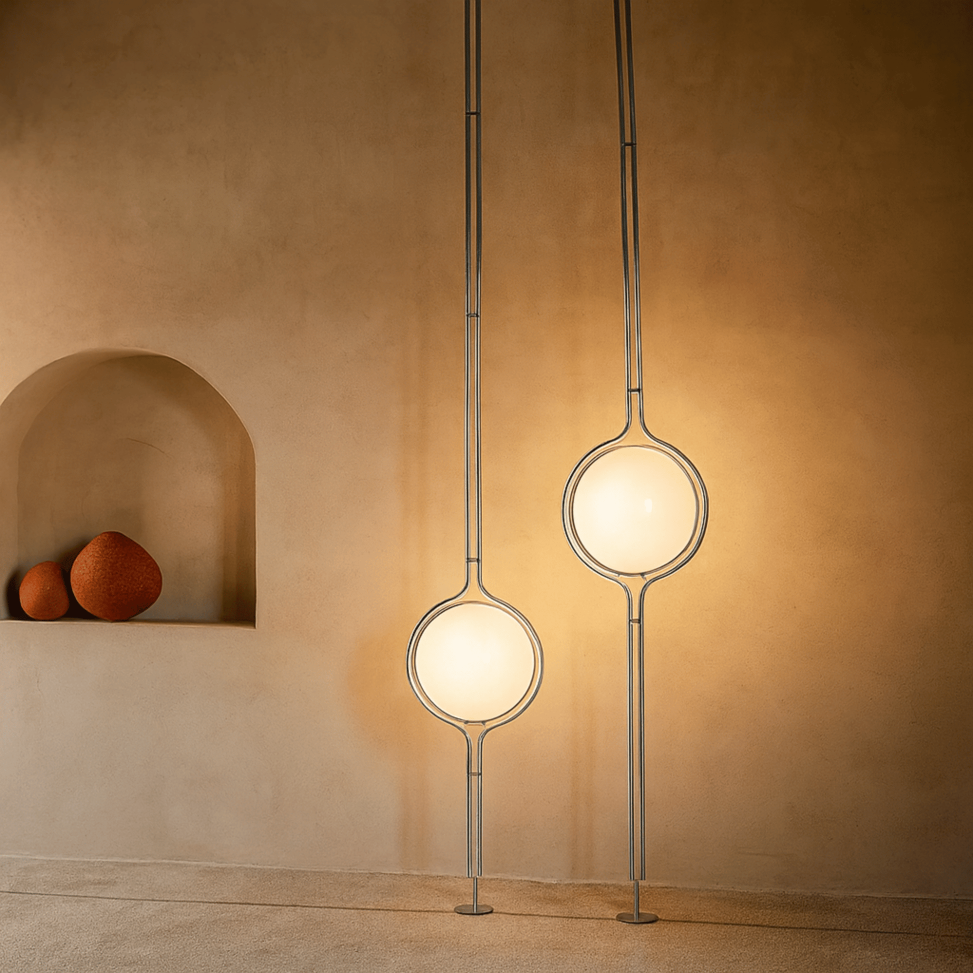 Two modern pendant lights hanging against a beige wall with a shelf displaying three spherical objects.