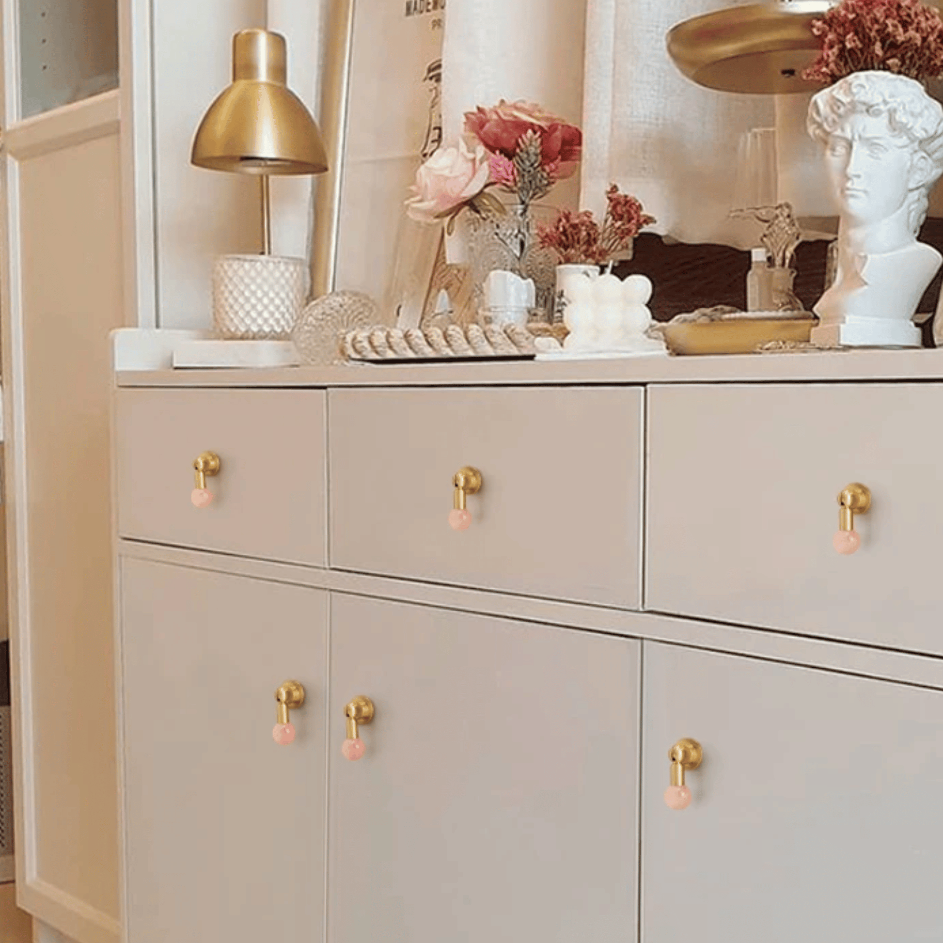 Beige cabinet with gold and pink knobs, decorated with flowers and a lamp.