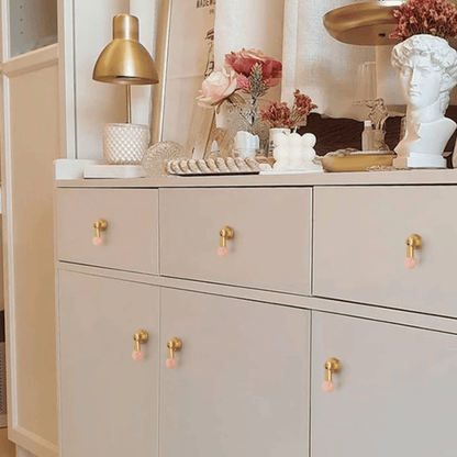 Beige cabinet with gold and pink knobs, decorated with flowers and a lamp.