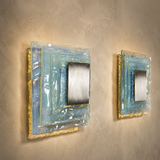 Two wall-mounted square mirrors with decorative frames on a textured wall.