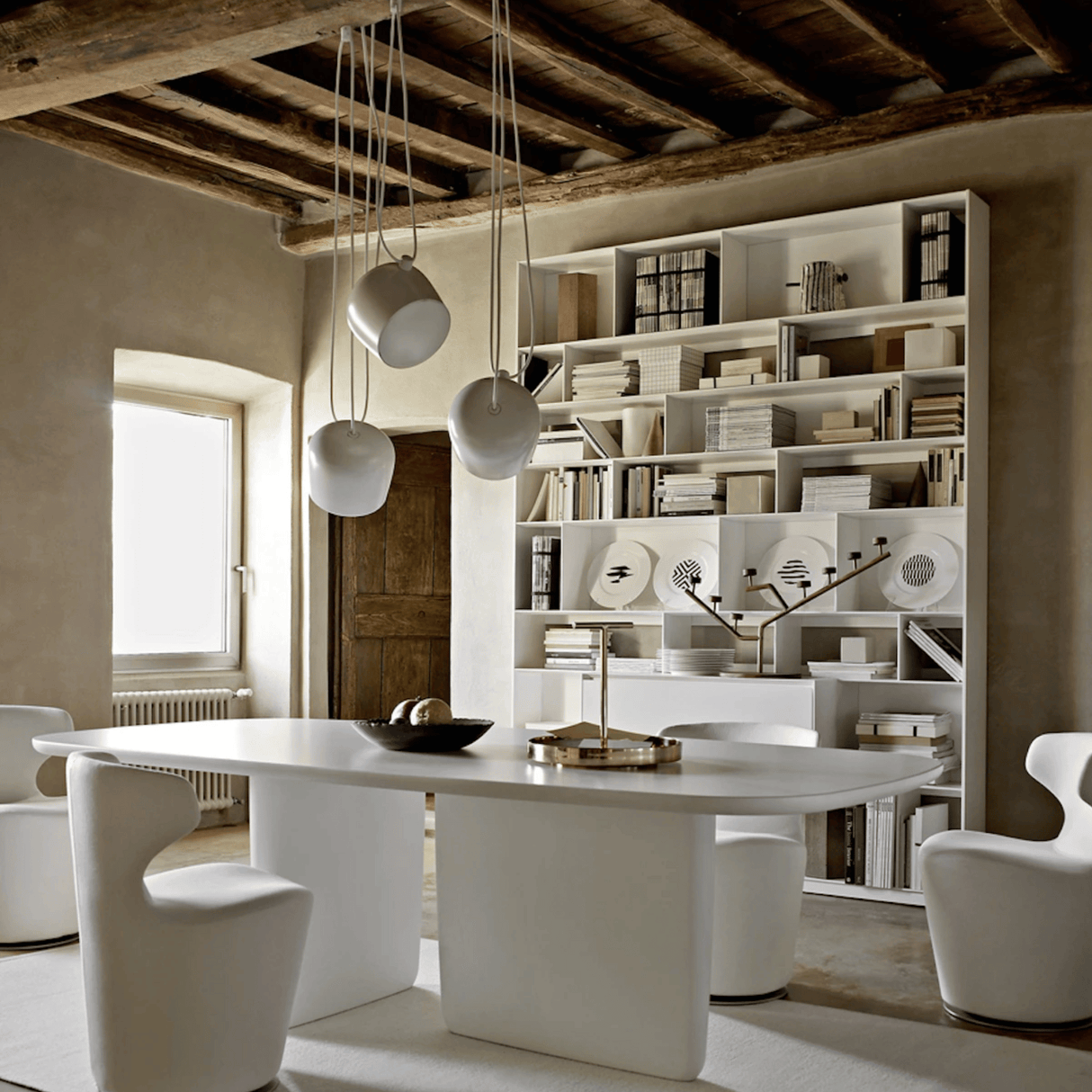 Modern dining room with a white table and chairs, bookshelf, and pendant lights.