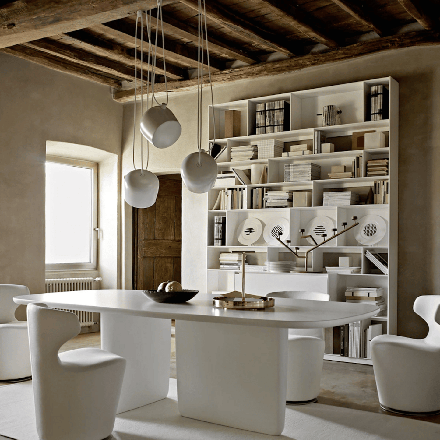 Modern dining room with a white table and chairs, bookshelf, and pendant lights.