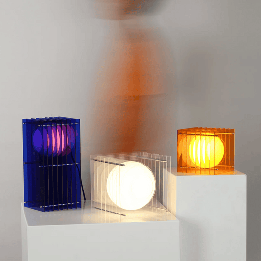 Three colorful cylindrical lamps on white stands against a gray background