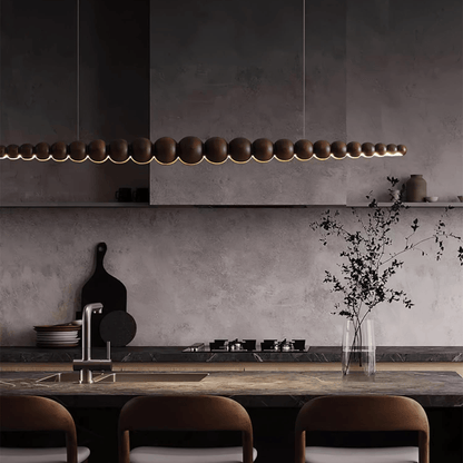 Modern kitchen with a long pendant light fixture, concrete wall, and wooden dining table.