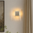 Square wall light fixture on a neutral wall with a painting and plant in the background
