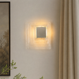 Square wall light fixture on a neutral wall with a painting and plant in the background