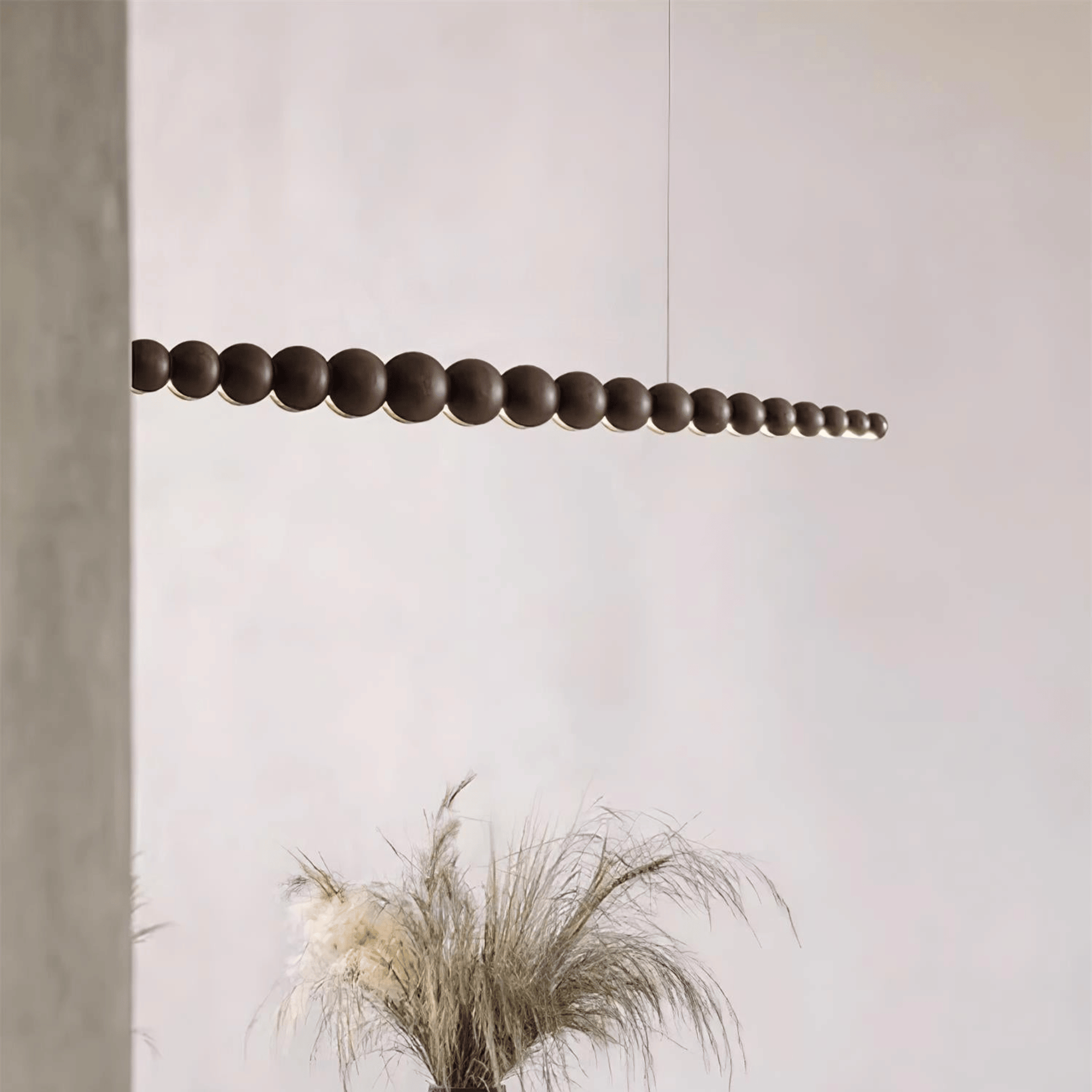Modern pendant light fixture hanging against a neutral wall with a plant in the foreground.