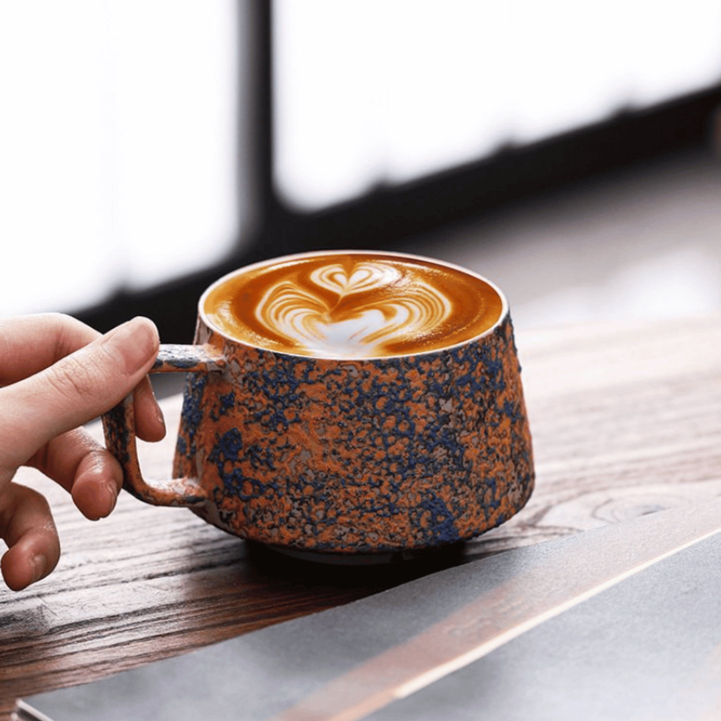 Hand holding a ceramic mug with latte art on a wooden surface