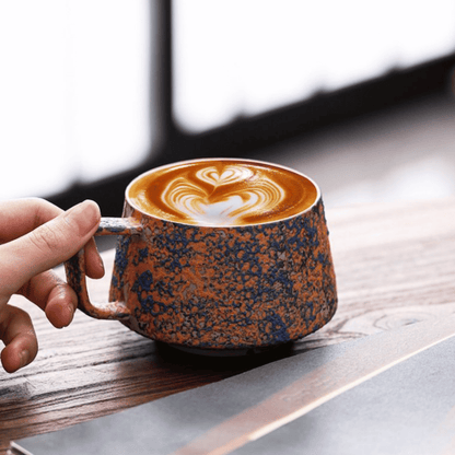 Hand holding a ceramic mug with latte art on a wooden surface