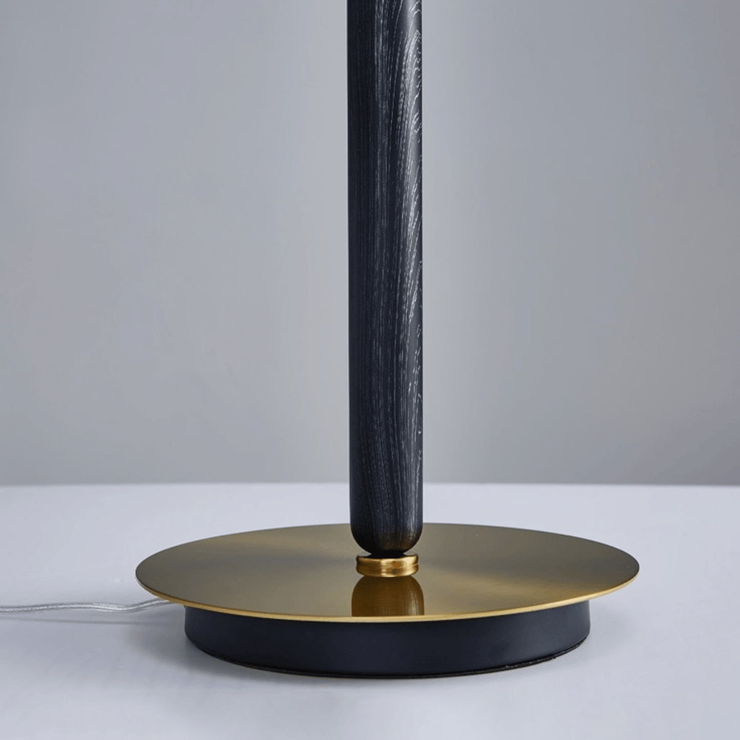 Table lamp with black cylindrical shade and gold base on a light gray background