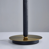 Table lamp with black cylindrical shade and gold base on a light gray background