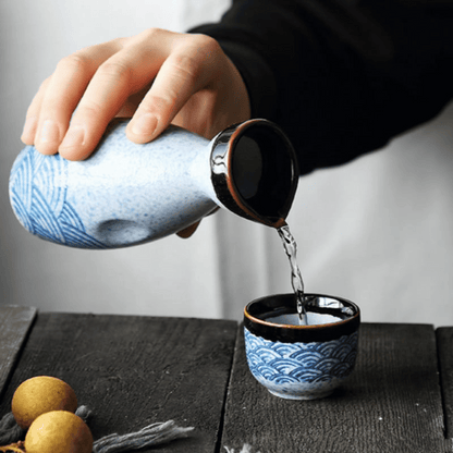 Ceramic teapot being poured into a matching teacup on a wooden surface.