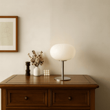 Table lamp on a wooden side table with decorative items against a beige wall.