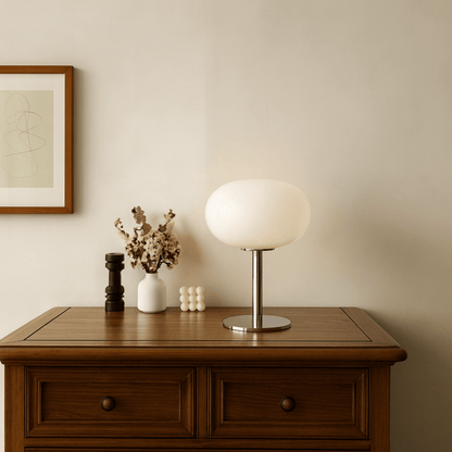 Table lamp on a wooden side table with decorative items against a beige wall.