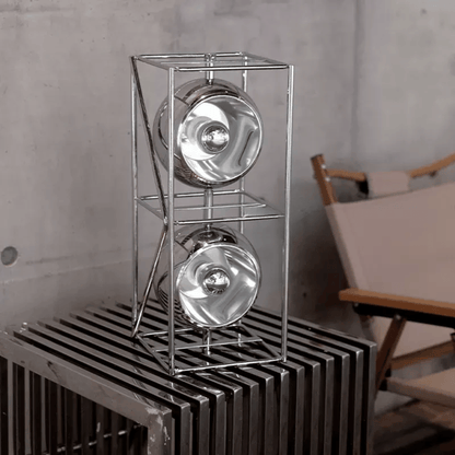 Metallic lampshades on a metal stand against a concrete wall.