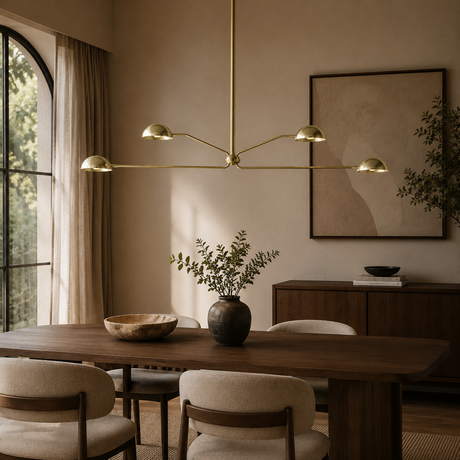 A modern brass multi-arm chandelier hangs over a wooden dining table in a warm, elegantly styled dining room with beige walls, upholstered chairs, and a large framed abstract print.