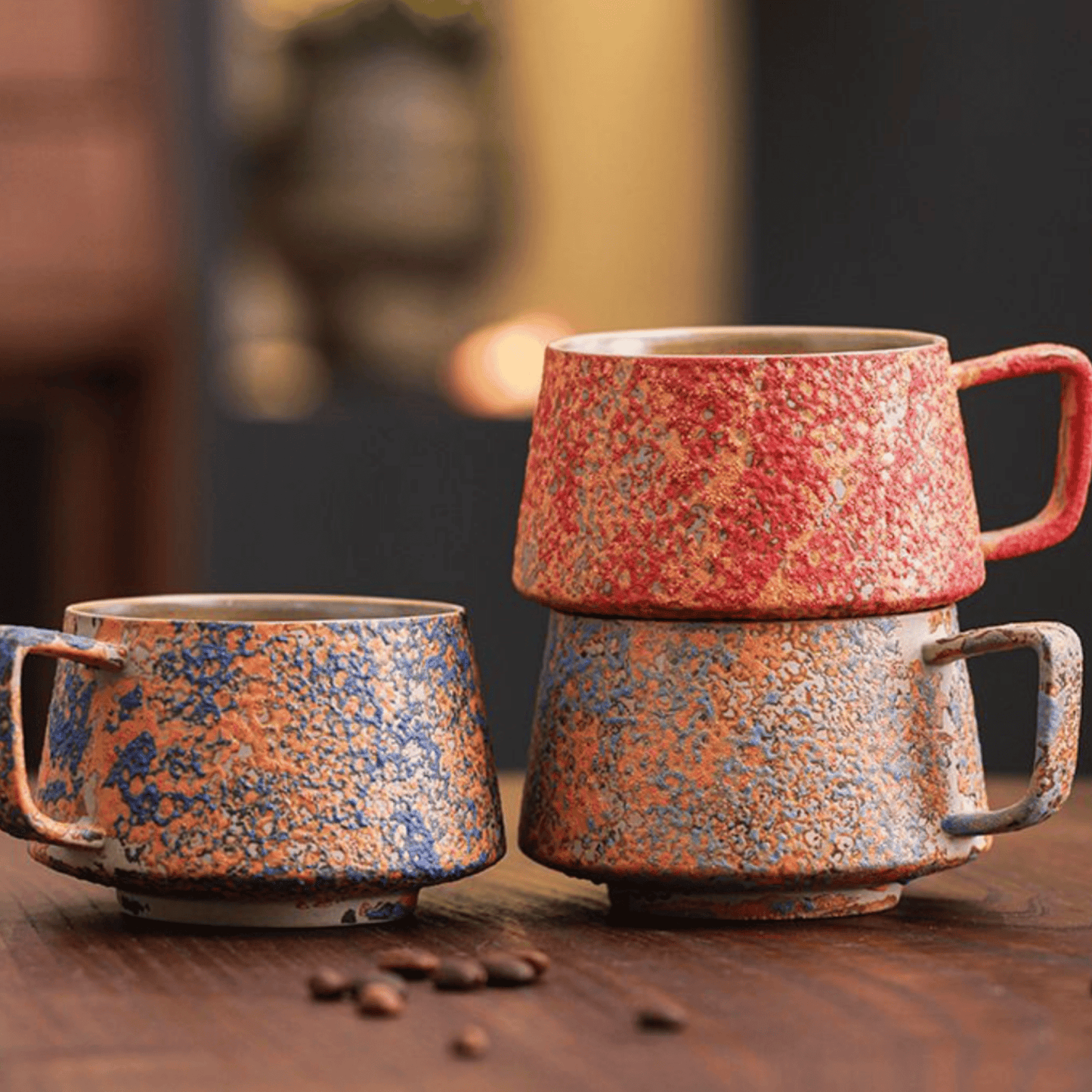 Three ceramic mugs with speckled patterns on a wooden surface with coffee beans.