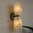 Wall-mounted light fixture with marble-like glass shades on a textured wall.