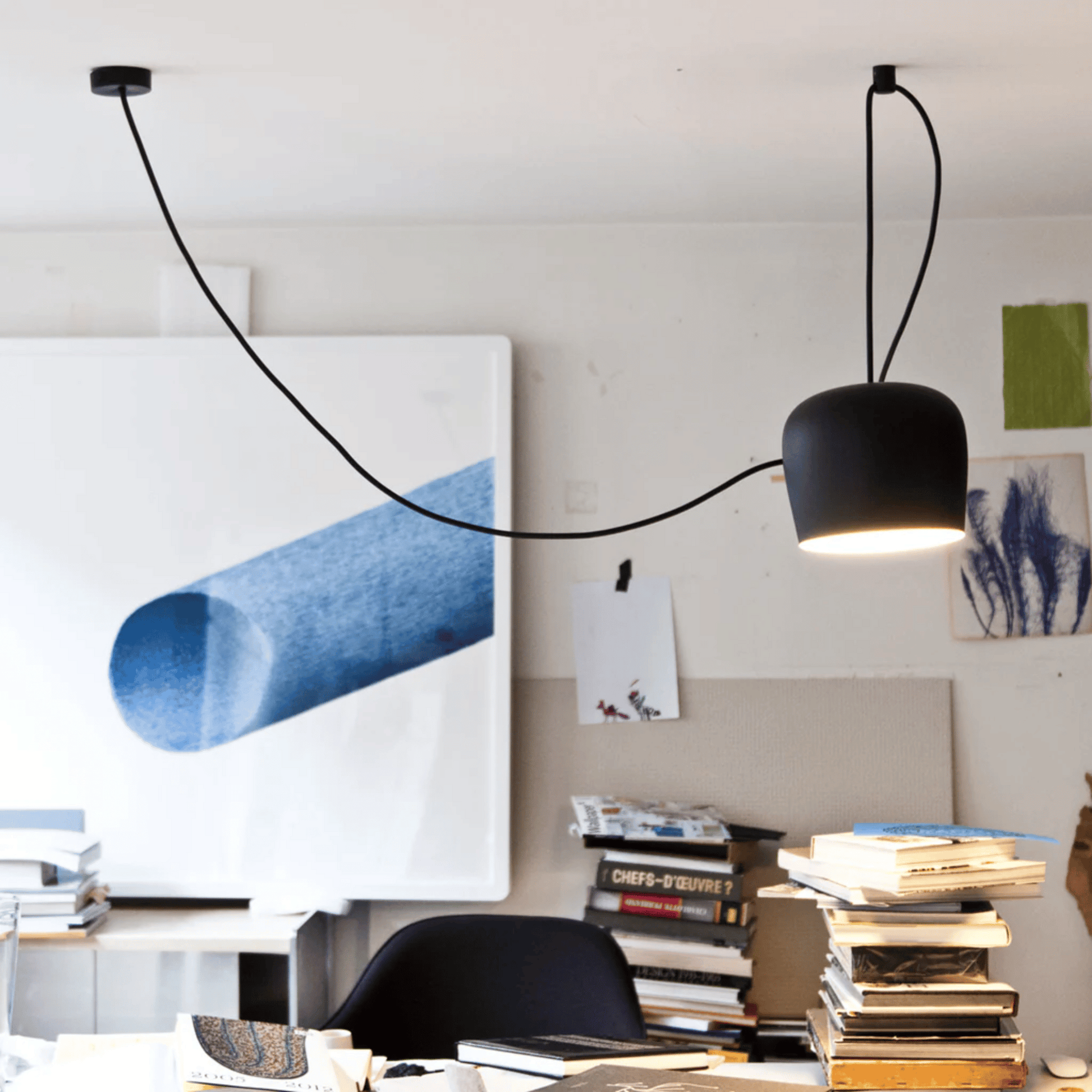 Modern black pendant light hanging in a room with books and artwork on the wall.