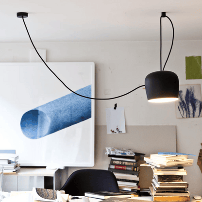 Modern black pendant light hanging in a room with books and artwork on the wall.