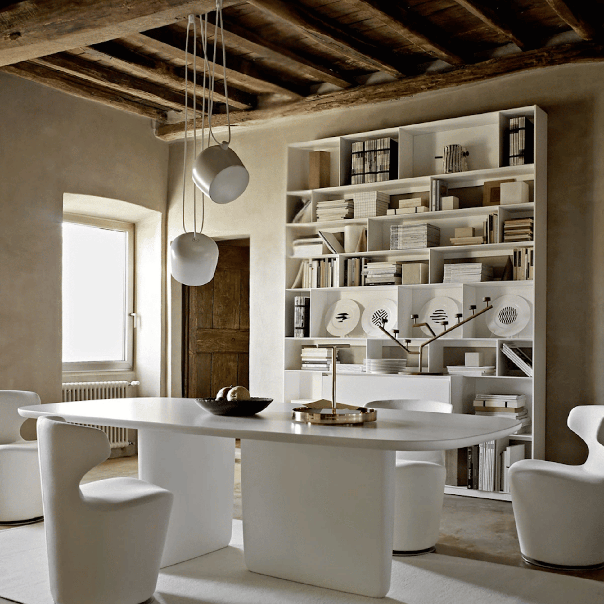 Modern dining room with a white table and chairs, bookshelf, and wooden ceiling.