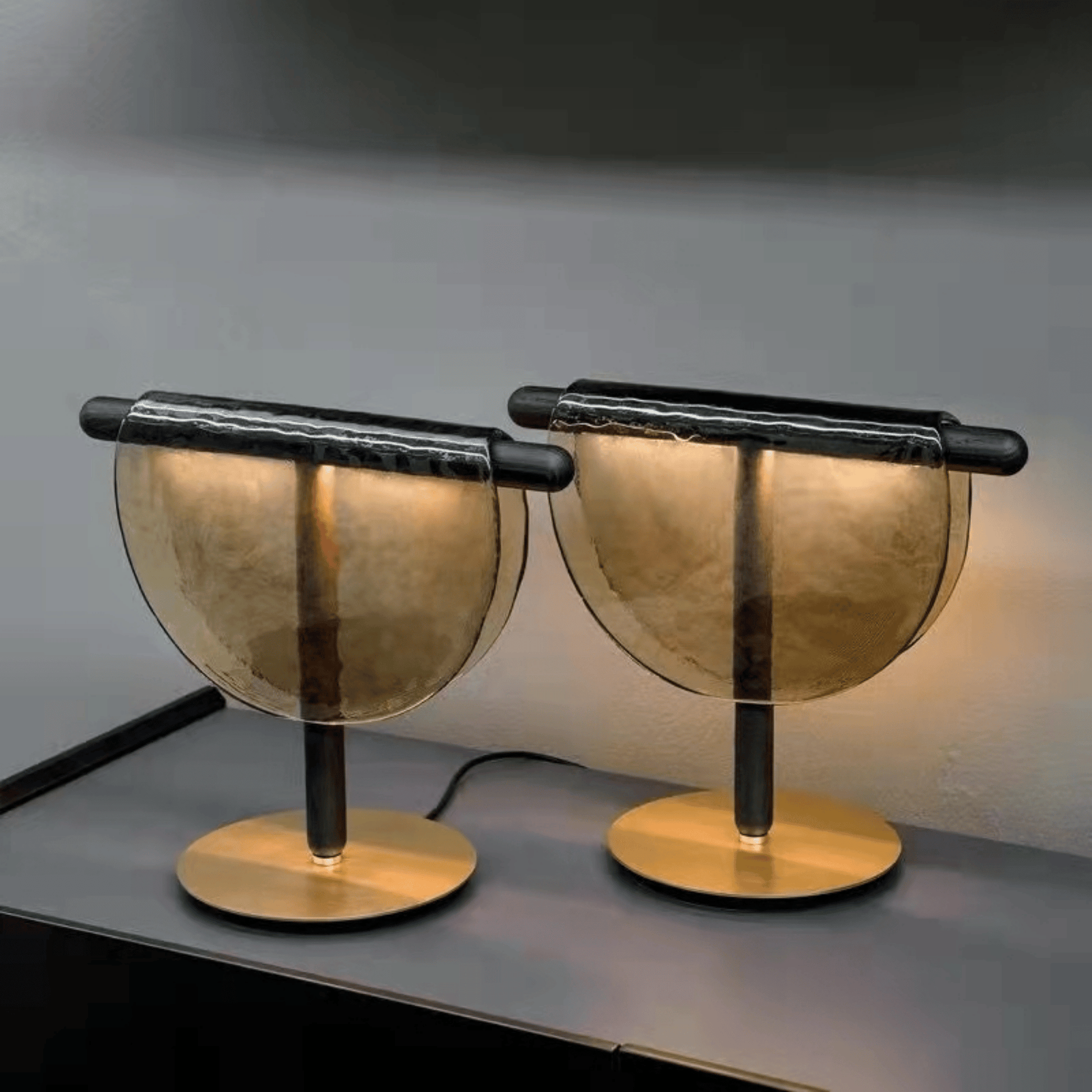 Two modern table lamps with gold and black design on a dark surface.