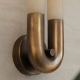 Brass wall sconce with two cylindrical lights on a neutral wall.